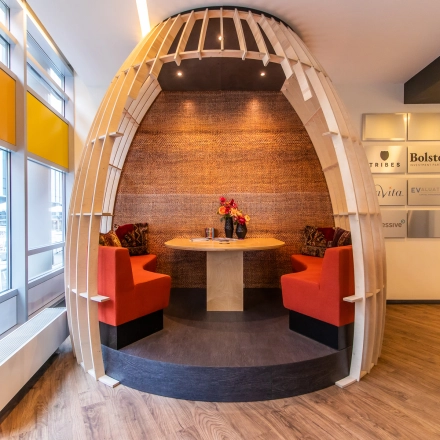 Cozy office space rental in Amsterdam Zuidas featuring a unique circular seating area with red cushioned benches and a wooden table, perfect for collaborative work sessions.