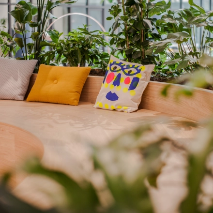 Modern office lounge area with colorful cushions on a wooden bench surrounded by greenery at Fred. Roeskestraat 100, Amsterdam Zuidas. Ideal for office space rental.