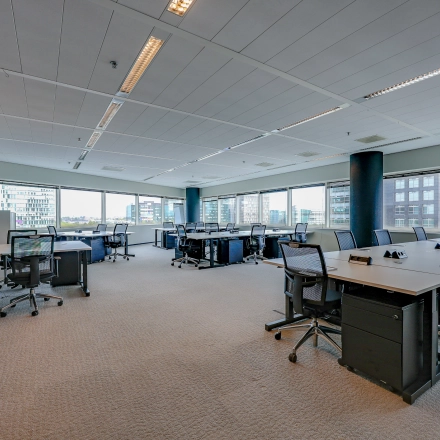 Bright office space available for rent at Gustav Mahlerplein, Amsterdam Zuidas, featuring modern desks, chairs, and large windows offering city views.