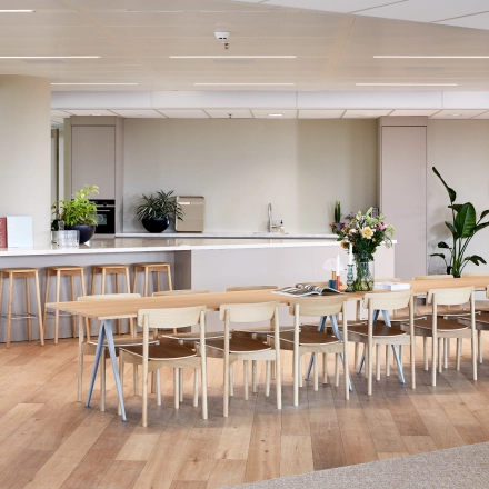 Spacious furnished office area in Amsterdam Zuidas, featuring a long table with chairs, bar stools, and a kitchenette. Ideal for office space rental at Hildegard Von Bingenstraat 44.