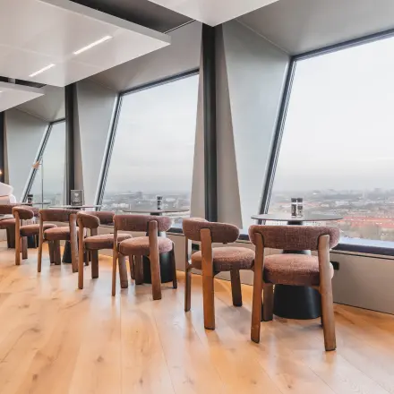 Bright office space with large windows overlooking Amsterdam Zuidas, featuring modern wooden furniture and city views. Ideal office space rental at Hildegard Von Bingenstraat 44.
