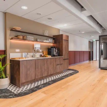 Furnished pantry area in an office space for rent at Hildegard Von Bingenstraat 44, Amsterdam Zuidas, featuring wooden cabinets and a coffee machine.