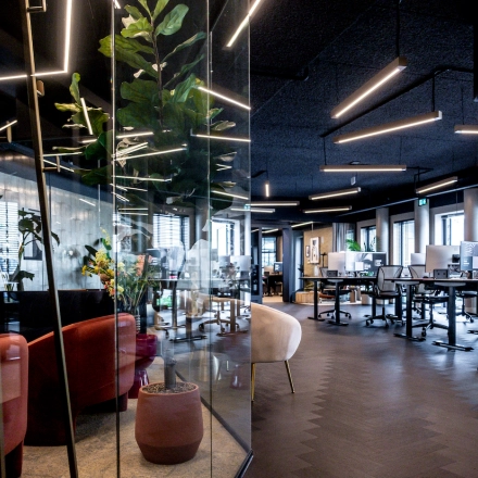 Modern office space with glass walls and stylish lighting; a mix of seating and workstations. Ideal for office space rental.