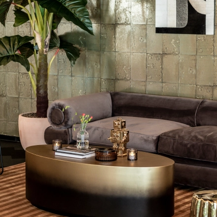 A stylish office lounge with a plush sofa, coffee table, decorative plant, and abstract artwork, located at Lange Amerikaweg 55-61, Apeldoorn. Ideal for office space rental.