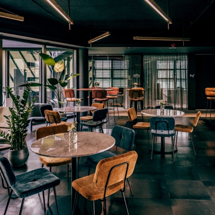 Stylishly furnished office space with round tables, multicolored chairs, and potted plants, ideal for rent at Lange Amerikaweg 55-61, Apeldoorn.