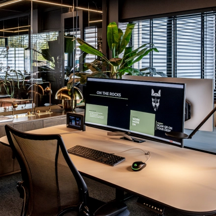 Modern furnished office space available for rent at Lange Amerikaweg 55-61, Apeldoorn. Features ergonomic chair, large monitor, sleek desk, and indoor plants, highlighting an inviting workspace atmosphere.