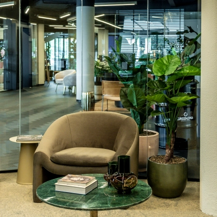 Rent office space at Lange Amerikaweg 55-61 in Apeldoorn featuring a cozy furnished lounge with glass walls, stylish seating, and greenery, ideal for office space rental.