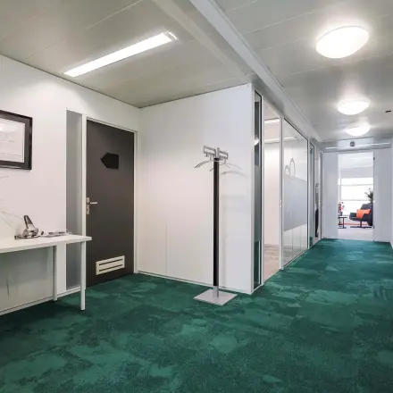 Bright office interior with green carpet, white walls, and a hallway leading to glass-partitioned rooms suitable for office space rental.