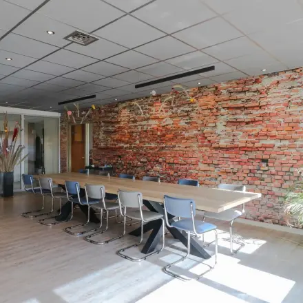 Spacious meeting room at Prins Willem-Alexanderlaan 401, Apeldoorn, featuring a long wooden table with chairs and a striking brick accent wall, available for office space rental.