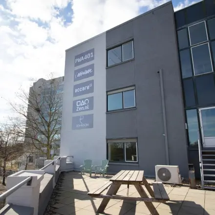Exterior view of the office building at Prins Willem-Alexanderlaan 401 in Apeldoorn with a terrace featuring a picnic table and outdoor chairs. Ideal for rent office space seekers.