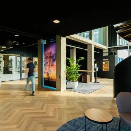 Spacious office entrance at Prins Willem Alexanderlaan 701, Apeldoorn, featuring modern decor with a spiral staircase and greenery. A person walks past the vibrant artwork.