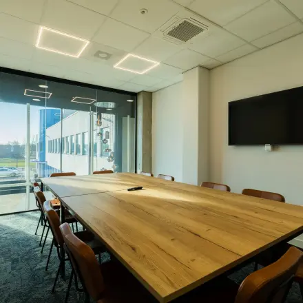 Modern conference room available for office space rental at Prins Willem Alexanderlaan 701, Apeldoorn, featuring a large wooden table, chairs, a wall-mounted screen, and a bright window view.