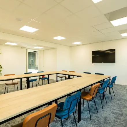Bright office space rental at Prins Willem Alexanderlaan 701, Apeldoorn, featuring a spacious meeting area with a large rectangular table, colorful chairs, and vibrant plants.
