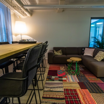 Cozy and vibrant office space at Jansbuitensingel 7, Arnhem Centrum, perfect for rent with a mix of seating options, colorful rug, and warm lighting.
