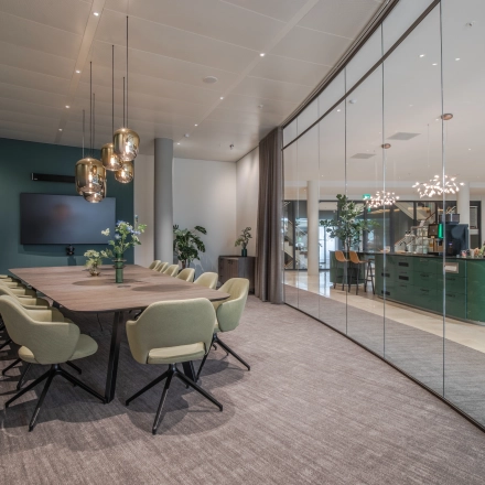 Stylish office space rental in Arnhem Zuid featuring a modern conference room with a long table and green chairs. Adjacent reception area visible through glass wall.