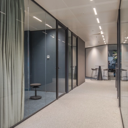 Modern office space for rent in Arnhem Zuid featuring glass-walled rooms with sleek furnishings and high ceilings.