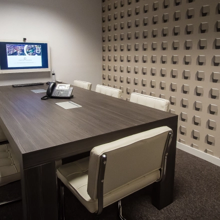 A furnished meeting room with a wooden table, chairs, and a wall-mounted screen at an office space rental on Carrer d'Aribau 161 in Barcelona Eixample.