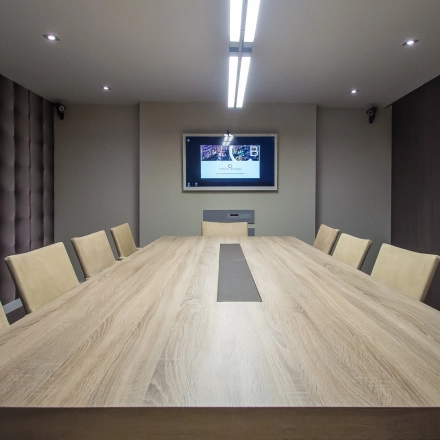 Modern conference room at Carrer d'Aribau 161, Barcelona Eixample with a large wooden table, cushioned chairs, and a wall-mounted screen, ideal for office space rental.