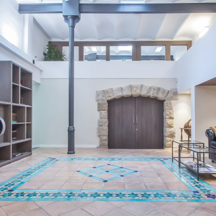 Spacious office space for rent in Barcelona Eixample, featuring stylish tiled flooring, a comfortable seating area, and large bookcases. Ideal for office space rental at Carrer d'Aribau 161.