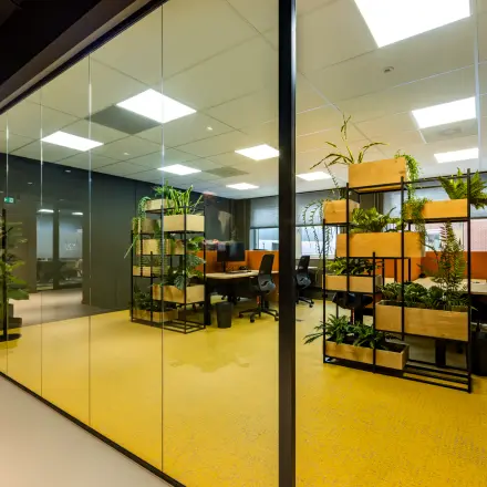 Bright office space with glass walls, modern furniture, and abundant plants at Baron van Nagellstraat 136, Barneveld. Ideal for office space rental with a vibrant and open-floorplan atmosphere.