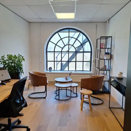 Bright office space at Zuidzijde Haven 39a, Bergen op Zoom, featuring a large arched window, wooden flooring, and modern furnishings, ideal for office space rental.