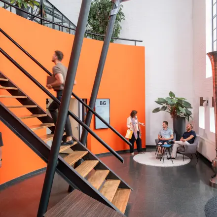 Bright office space with modern staircase at Zuidzijde Haven 39a, featuring professionals conversing and using devices. Ideal for rent office space seekers.