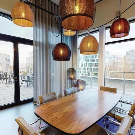 Spacious office space rental in Berlin Friedrichshain with a large conference table, stylish chairs, and modern lighting. Windows open to a scenic balcony view.