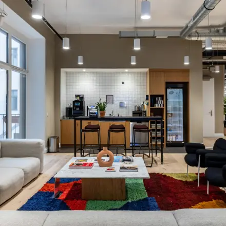 Spacious Berlin Kreuzberg office to rent with a stylish lounge area, featuring cozy armchairs, a vibrant rug, and a modern kitchen space.