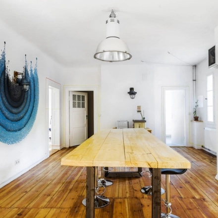 Berlin Lichtenberg office space rental at Blockdammweg 1 with a unique wall art, wooden flooring, and modern furnishings. Ideal for an office to rent with natural light and stylish decor.