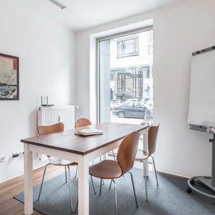 Bright, minimalist office to rent at Jägerstraße 63 D, Berlin Mitte, featuring a table with chairs and a flip chart, ideal for small meetings or office space rental.