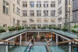 A glass-roofed atrium in an office building at Krausenstraße 9, Berlin Mitte, showcasing greenery and a person walking down the stairs. Ideal for office space rental.