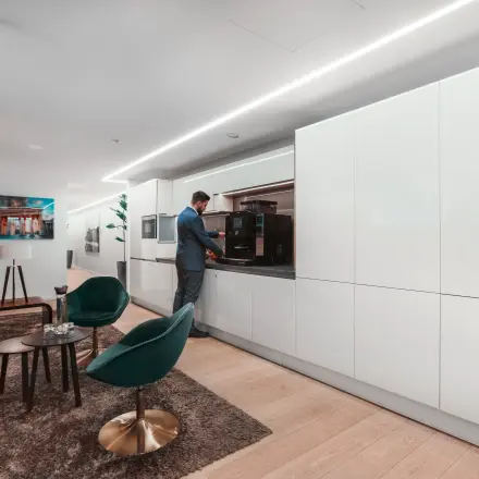 A modern, furnished office space at Pariser Platz 6a, Berlin Mitte, featuring a lounge area and a person using a coffee machine. Ideal for those looking to rent office space.