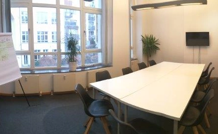 Spacious and bright conference room available for office space rental in Berlin Mitte, featuring a large table, chairs, and a whiteboard.