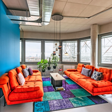 Bright office lounge with orange couches and colorful rugs, located at EUREF-Campus 22, Berlin Schöneberg, ideal for office space rental.