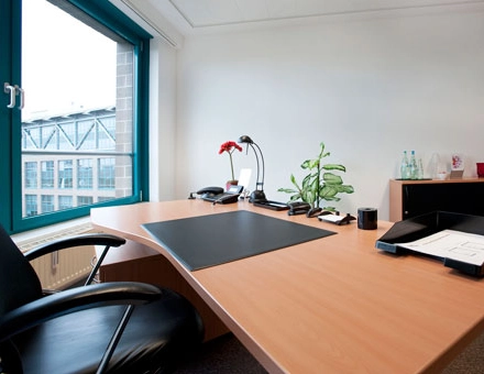 A furnished office space at Flughafenallee 26, Bremen Neustadt, featuring a desk with office supplies, a chair, and a large window offering natural light. Ideal for office space rental.