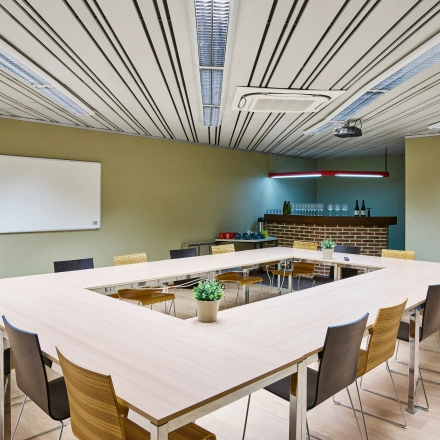 Spacious conference room for office space rental at Leuvensesteenweg 613, featuring U-shaped table setup, chairs, whiteboard, and a small bar area in Brussels Airport.