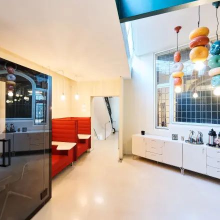 Bright office space with modern furnishings and playful lighting in Rue du Congres 37, Brussels Center, available for rent. Includes workspaces and a coffee station.