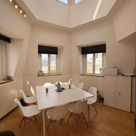 Bright office space with a central table and chairs under a skylight, ideal for office space rental in Brussels Center.