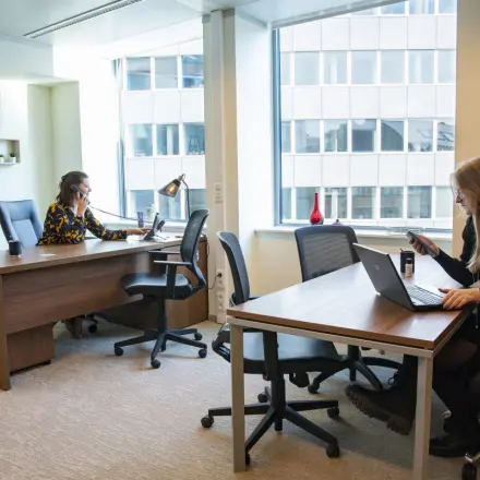 Professionals engaged in work at a bright, furnished office space in Brussels European District. Ideal for those considering office space rental at Robert Schumanplein 2-4.