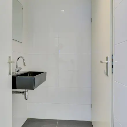 Minimalistic restroom with a sleek black sink and white tiled walls at Regulierenring 2, ideal for office space rental.