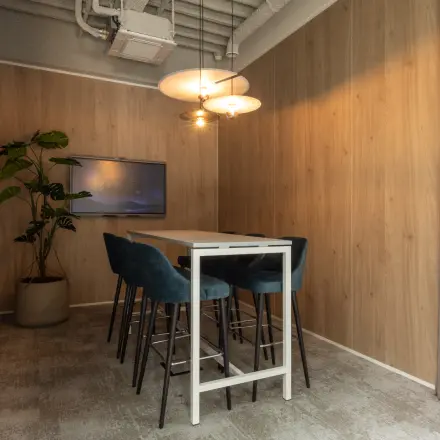 Furnished office space for rent at Essebaan 63, Capelle aan den IJssel, featuring a high table with chairs, wooden walls, and a screen for presentations.