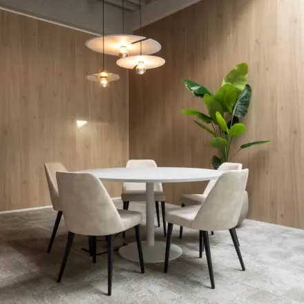 Cozy office space rental with round table, chairs, modern lighting, and a plant in a wood-paneled room at Essebaan 63.
