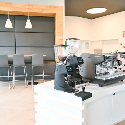 A bright kitchen area with a person making coffee, featuring modern bar stools and light wood accents, ideal for office space rental.