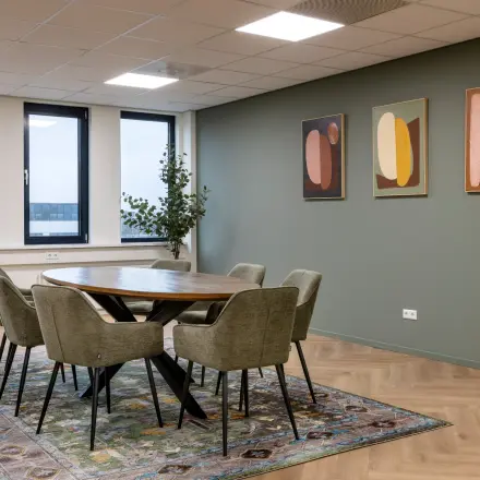 Modern office space at Vlierbaan 20, Capelle aan den IJssel, featuring a round table with chairs on a patterned rug, and abstract art on the wall.