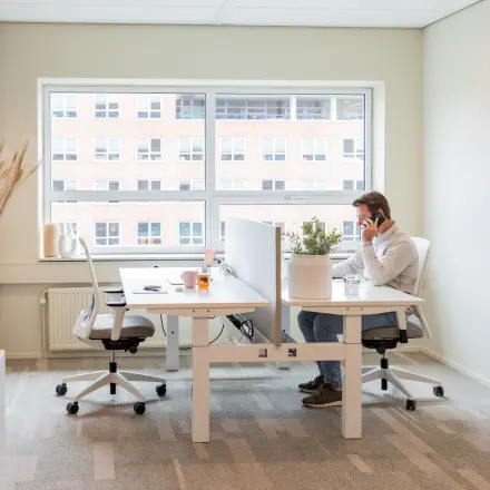 Bright office space at Rijnzathe 12, De Meern, featuring modern desks and chairs. A person is engaged in a phone call, showcasing active business use. Ideal for office space rental.