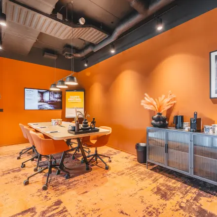 Modern office space with bold orange walls, a large table, and chairs, ideal for office space rental at Rijnzathe 12, De Meern.