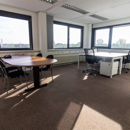 Bright office space for rent at Marshalllaan 2, Delft, featuring large windows, desks, and chairs suitable for a productive work environment.