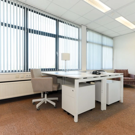 A well-lit, furnished office space for rent at Marshalllaan 2, Delft, featuring modern desks and chairs with large windows providing ample natural light.
