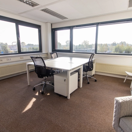 Bright office space at Marshalllaan 2, Delft, featuring large windows with a pleasant view, equipped with desks and chairs for rental office space needs.