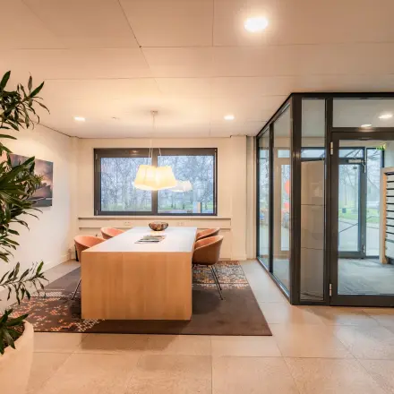 A tastefully furnished office to rent at Marshalllaan 2, Delft, featuring a sleek conference room with a large table, comfortable chairs, and bright lighting. Ideal for office space rental.